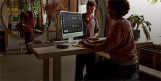 شخصان في غرفة مضاءة جيدًا، يشاهدان المنتجات على شاشة iMac الزجاجية ذات الملمس النانوي