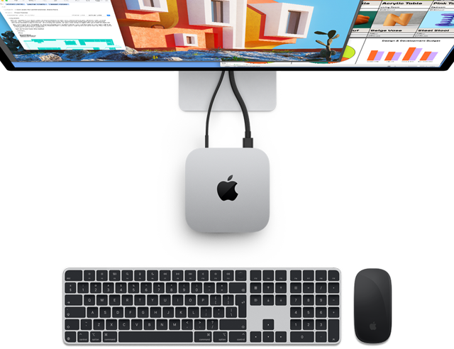 أعلى جهاز Mac mini الفضي الذي يحمل شعار Apple، يظهر متصلاً بشاشة وبجوار لوحة مفاتيح Magic Keyboard وMagic Mouse اللاسلكية